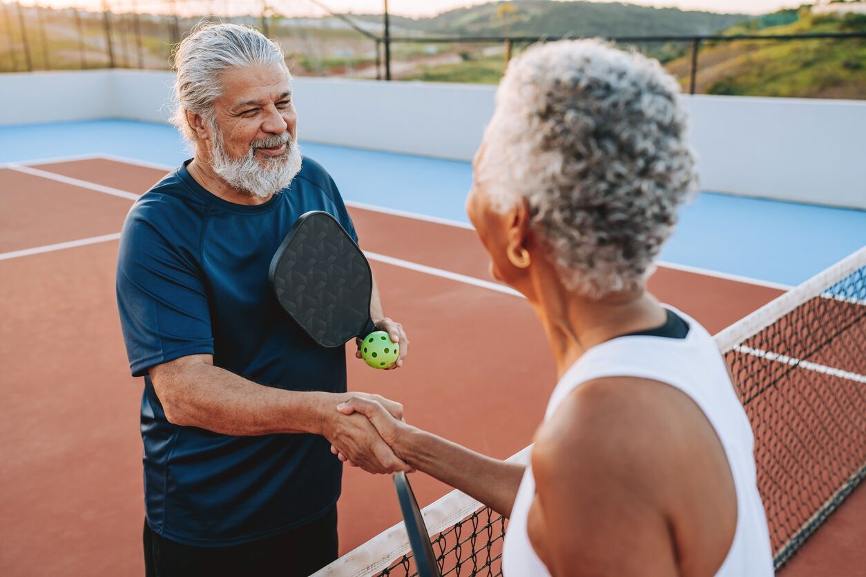 Two seniors shake hands after an outdoor pickleball game