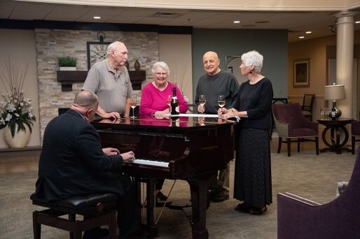 A group of friends gathers around a piano with drinks in hand.